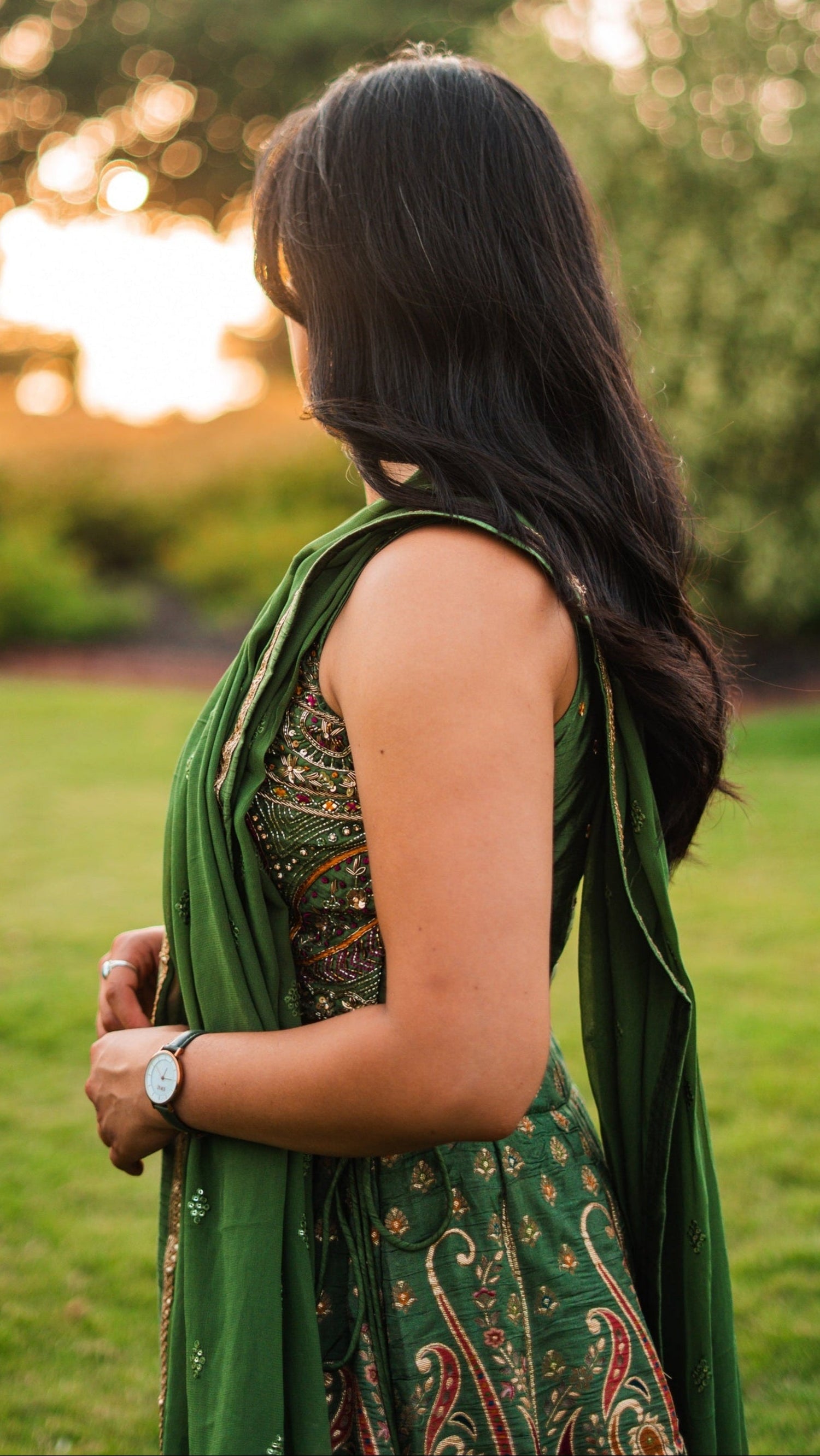 Woman in a Indian Sari Dress with a patterned shawl standing in a grassy field with a sunset in the background.